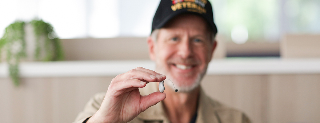 Image of a male veteran holding up a hearing aid